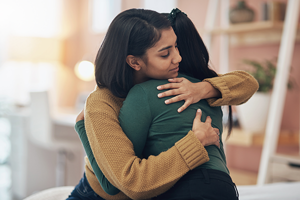 Stock image of two young women hugging in support of one another after having a youth peer counseling session